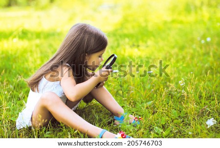 Little girl looking through a magnifying glass on flower