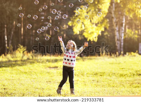 Little child having fun with bubbles soap in sunny autumn day