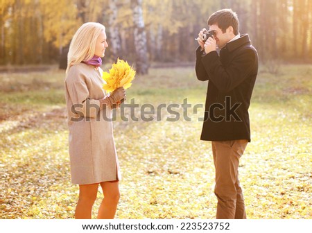 Autumn, love, relationships and people concept - happy couple having fun outdoors man photographing on retro vintage camera woman in autumn park