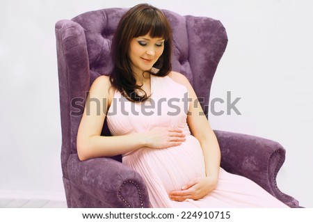 Pregnancy, motherhood and happy future mother concept - beautiful pregnant woman sitting on armchair