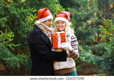 Christmas and people concept - man giving a box gift to a woman, happy pretty couple in love against christmas tree in winter