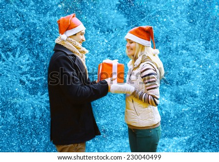 Christmas and people concept - happy man giving a box gift to a woman, happy pretty couple in winter snowy day