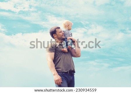 Lifestyle atmospheric portrait happy father and son having fun outdoors against blue sky with clouds, soft vintage pastel colors