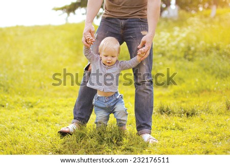Father helping baby doing first steps in summer day