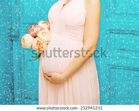 Christmas, pregnancy, motherhood and people concept - lovely beauty pregnant woman in dress with bouquet flowers against the snowflakes
