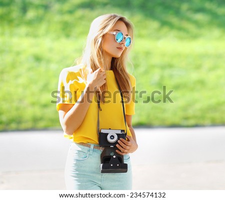 Summer portrait stylish pretty hipster girl in sunglasses with retro vintage camera posing in city, street fashion