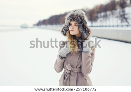 Portrait of a beautiful woman dressed a coat and fur hat in the winter field