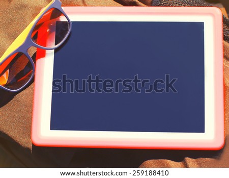 Fashion and technology concept - empty screen tablet pc and sunglasses on the backpack, top view