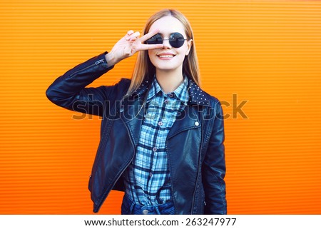 Fashion outdoor portrait of pretty cool girl in trendy rock style having fun against a colorful orange urban wall
