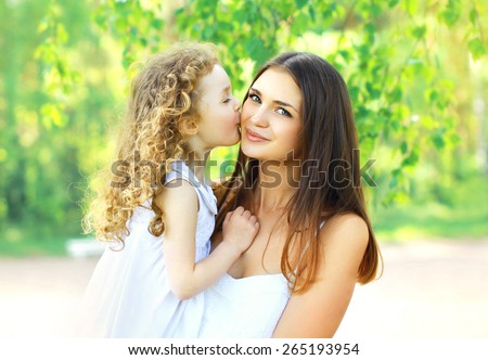 Mother\'s day, family, childhood and people concept - loving daughter kissing mother, happy young mom and child in warm sunny summer day on the nature