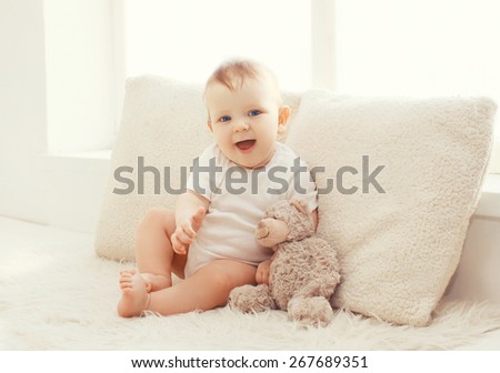 Baby with teddy bear at home in white room near window