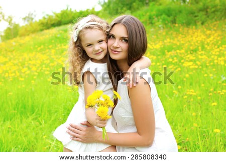 Sunny portrait of mother and daughter together with yellow dandelion flowers in summer day, mom with child outdoors