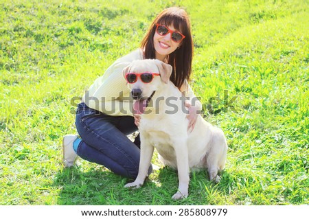 Happy owner woman with labrador retriever dog in sunglasses on the grass in summer day