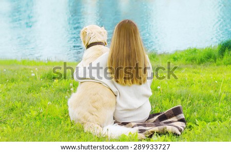 Silhouette of owner and Golden Retriever dog sitting together on the grass near river in sunny summer day