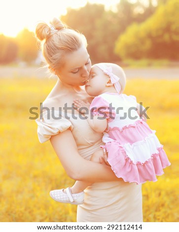Sunny portrait of happy mom kissing baby on hands in sunny evening with sunset