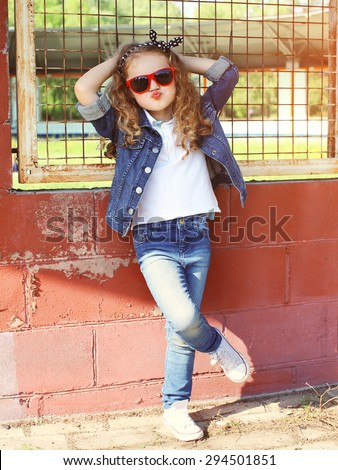 Fashion kid concept - stylish little girl child wearing a jeans clothes and sunglasses posing summer in the city