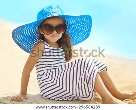 Summer, vacation and travel concept - portrait of pretty little girl in a striped dress and straw hat relaxing resting on the beach near sea