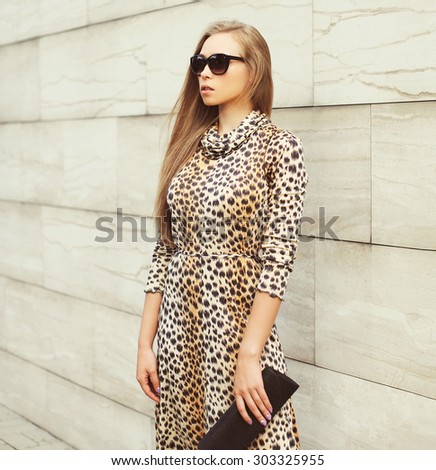 Fashion beautiful blonde woman wearing a leopard dress and sunglasses with handbag clutch in the city