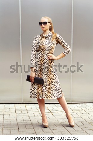 Fashion beautiful woman wearing a leopard dress and sunglasses with handbag clutch in the city