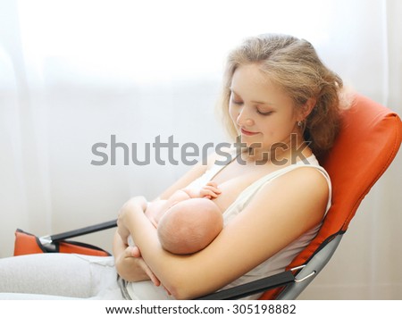 Happy mom holding on hands baby and feeding breast at home