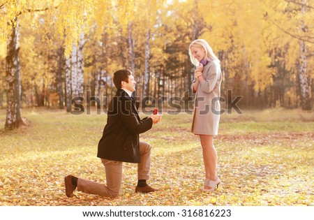 Kneeled man proposing ring to a woman in autumn park