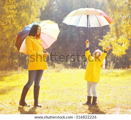Happy family with umbrellas in sunny autumn rainy day, mother and child enjoying rain
