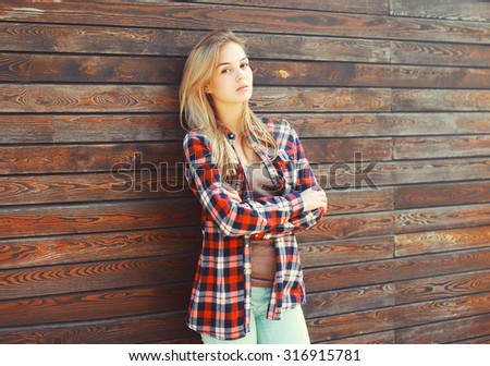 Fashion young blonde woman in checkered shirt over brown wooden background