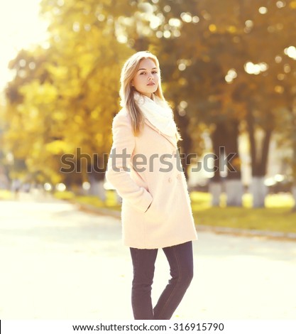 Beautiful young woman wearing a pink coat in sunny autumn park