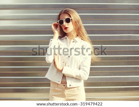Fashion portrait stylish woman in sunglasses and white denim jacket over metal textured background