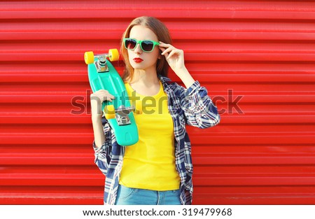 Fashion pretty cool girl wearing a sunglasses with skateboard and colorful clothes over red background