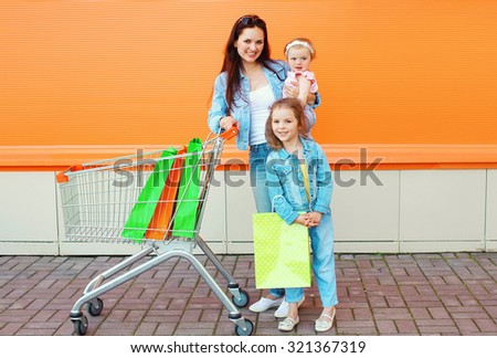 Happy mother and two children with trolley cart and colorful shopping bags
