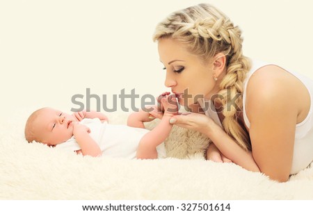 Loving mother kissing feet baby on bed at home