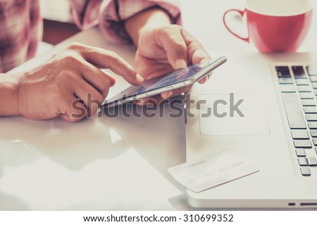 Man\'s hands holding a credit card and using smart phone for online shopping