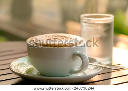 blur focus a cup of coffee and glass of water backlight made with vintage tone