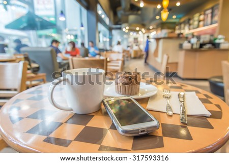 Blurred coffee shop,Vintage filter,A cup of coffee ,mupfin cake and smart phone on the wood table