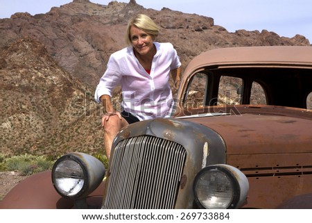 Mature, active, senior woman riding antique car in desert