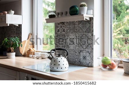 Modern kitchen with grey design tiles and wooden furniture. Big window and plant in scandinavian interior of kitchen. Cozy home in white color.