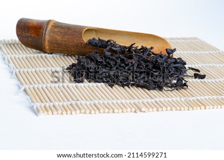Oolong tea 'Big red robe' wildly known under original chinese name 'Da hong pao 大红袍 '  with wooden spoon on bamboo mat,  white background close-up, copy space, side view. 商業照片 © 