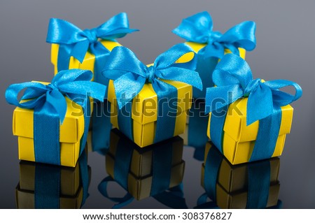 Yellow gift boxes with blue satin ribbons on the mirror dark background