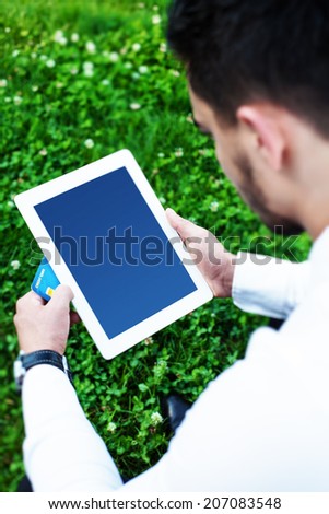 Young business man sitting in city park holding computer tablet