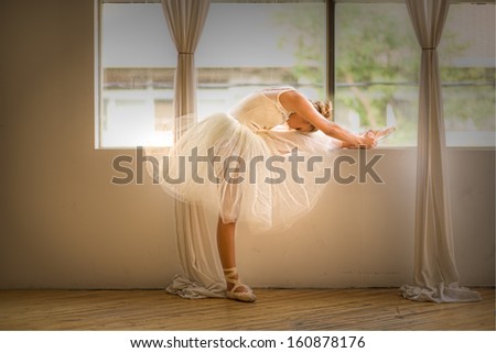 teen girl ballet dancer stretching beside a window