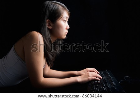 young attractive asian woman laying on a black background working on a computer