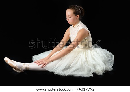 teen girl ballet dancer sitting in a tutu in points on a black background