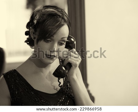 Sepia tone retro photo of a woman in a flapper dress and head dress talking on an old telephone.