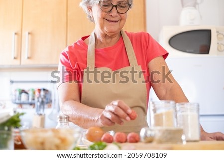 Senior woman preparing fresh meatballs ready to be cooked, wooden cutting board and raw ingredients Foto stock © 