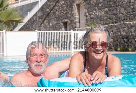 Happy senior couple laughing in the swimming pool relaxing tunning on inflatable mattress. Happy retired people enjoying summer vacation doing healthy activity Stock foto © 