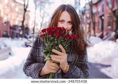 Young woman admiring red roses on a winter background
