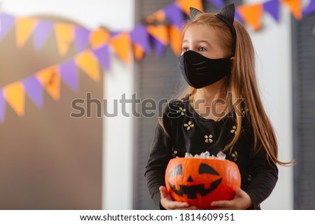 A girl in a Halloween costume with a mask on is holding a pumpkin filled with treats during the covid19 pandemic at a Costume Party.