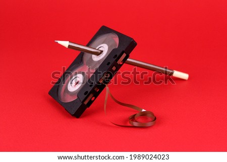 Old audio cassette with a pencil in the hole on a red background. Old rewind cassette tape with tape by pencil