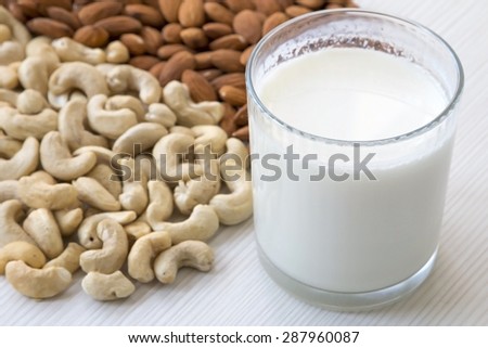 Closeup Nut Milk. Cashew Nuts and Almond Nuts with Glass of Walnut Milk on White Wooden Background.